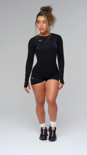 Woman wearing a black MG Wear long-sleeve romper and white sneakers, studio.
